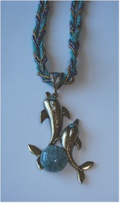 Twisted silk and beaded cords hold two silvery dolphins with turquoise eyes